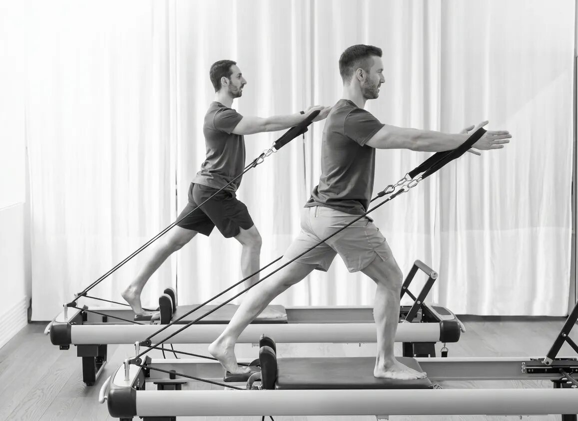 Two people practising Pilates on reformer machines